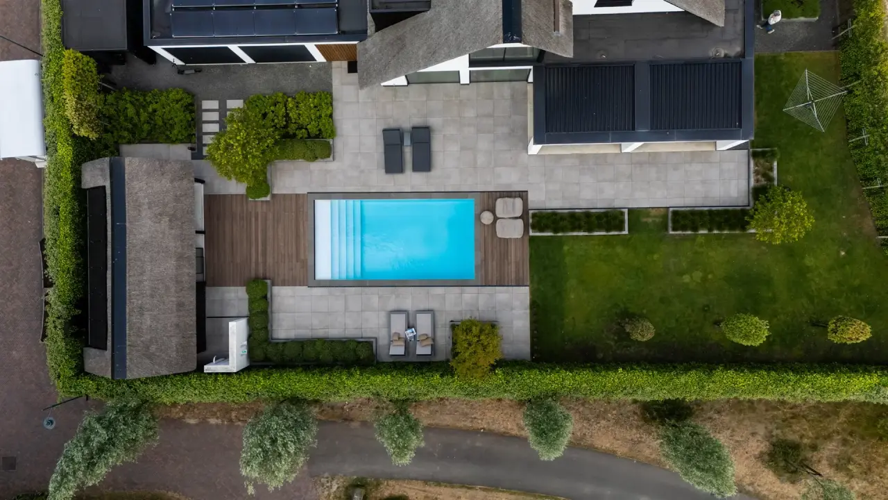Vogelvlucht van tuin met strak rechthoekig zwembad en overdekte zithoek.