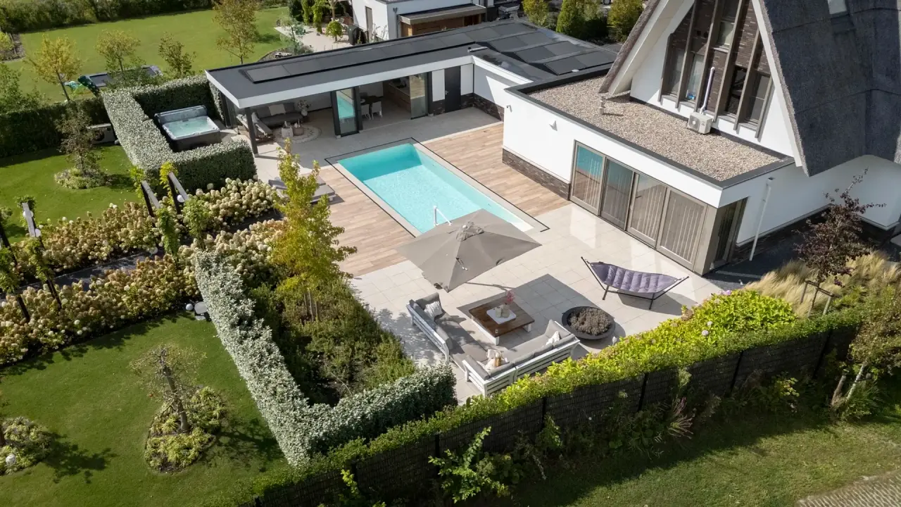 Ruim tuinontwerp met zwembad, terrassen en stijlvolle beplanting rond de woning.