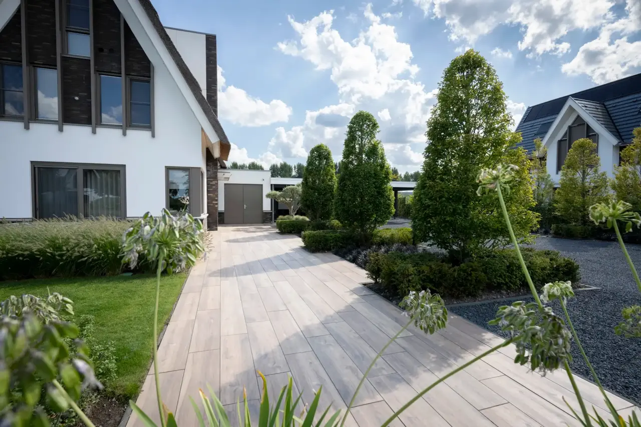 Verhard pad tussen woning en tuin met zicht op de border en het gazon.