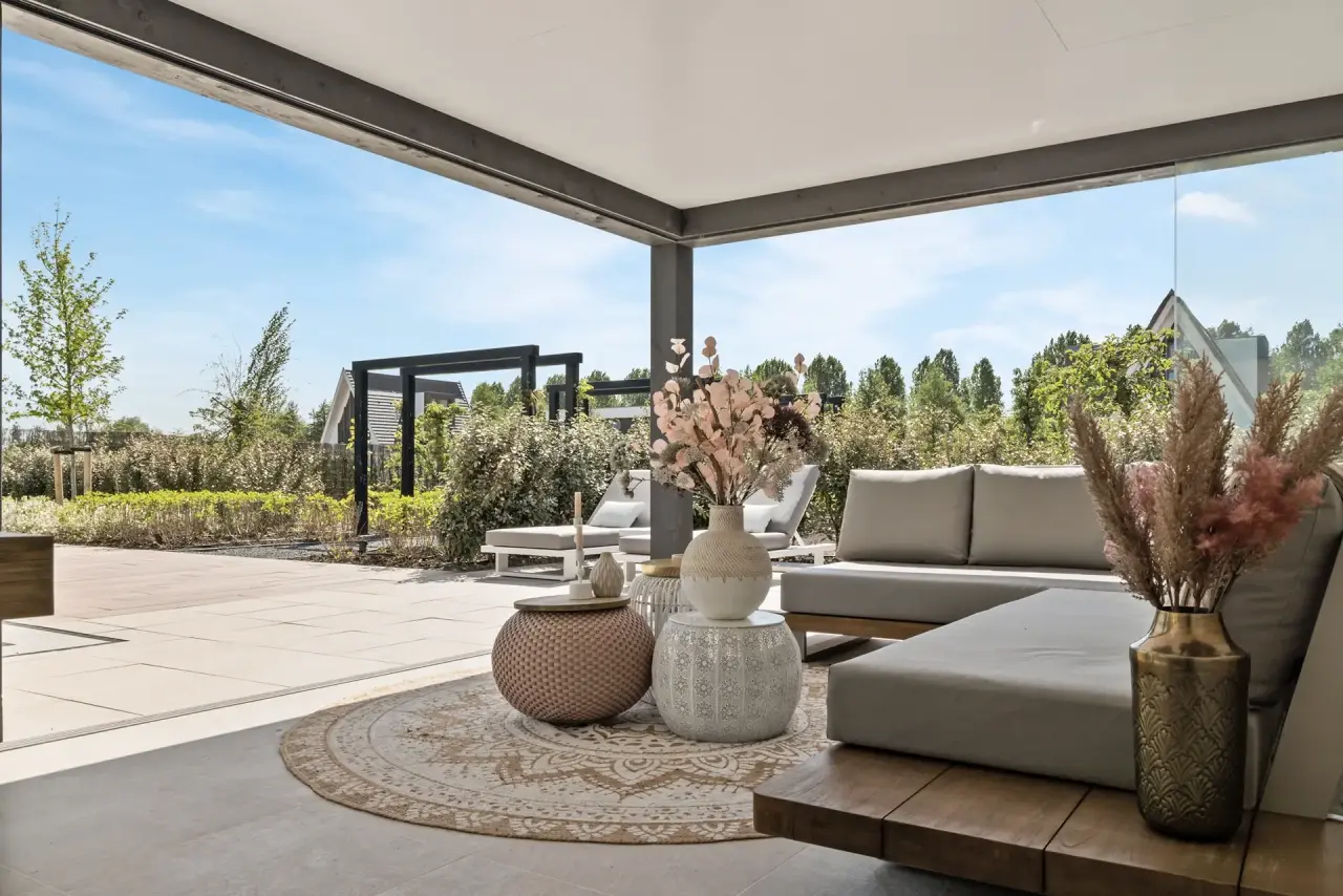 Terras onder lamellendak met comfortabele zithoek en uitzicht over de tuin.