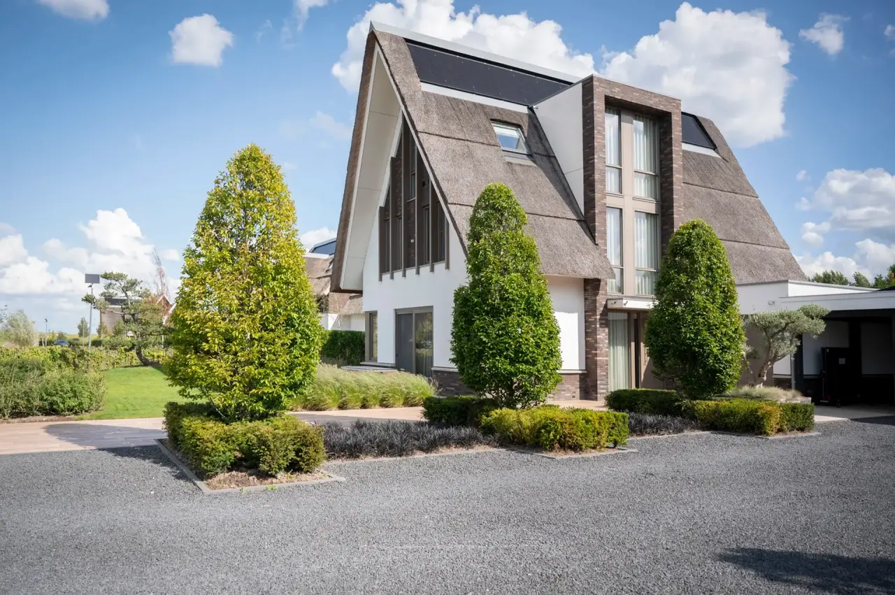 Voorzijde van de woning met oprijlaan, hagen en symmetrische beplanting.