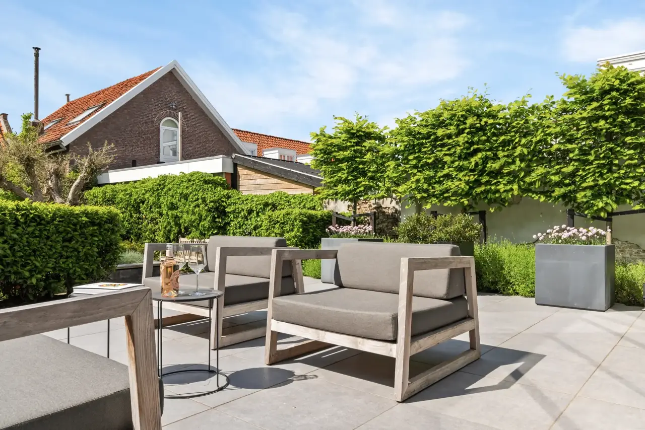 Zithoek met moderne tuintafel naast haag en beplanting.