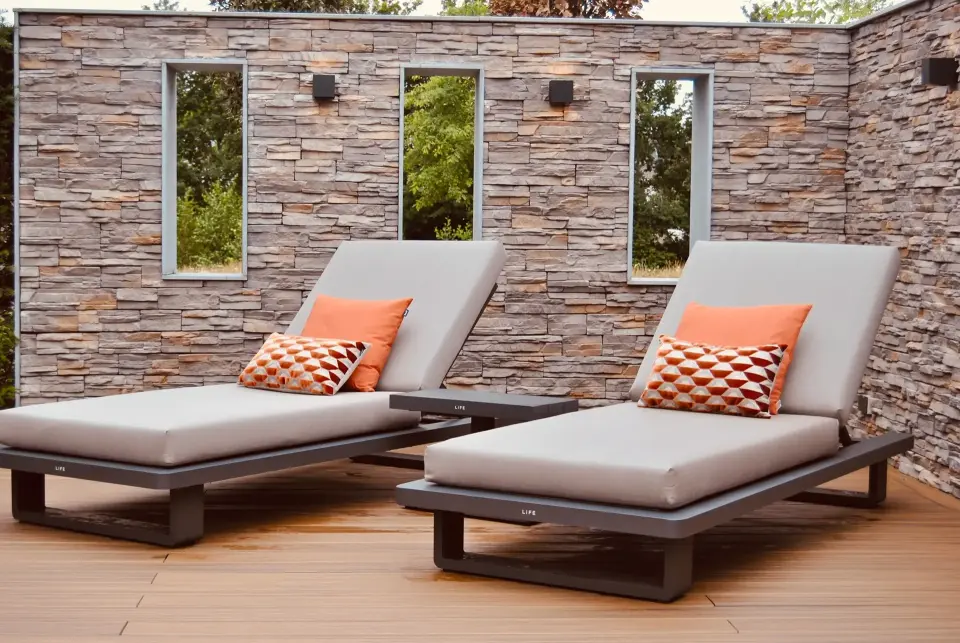 Stijlvol terras met moderne ligbedden en natuurstenen wand, ontworpen door Art Verde