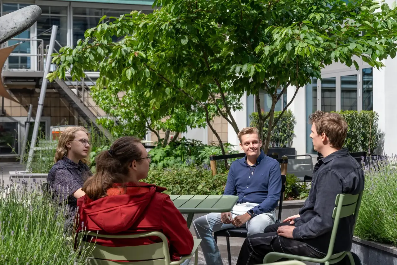 Studenten genieten van de zon op het terras tussen de groene beplanting.