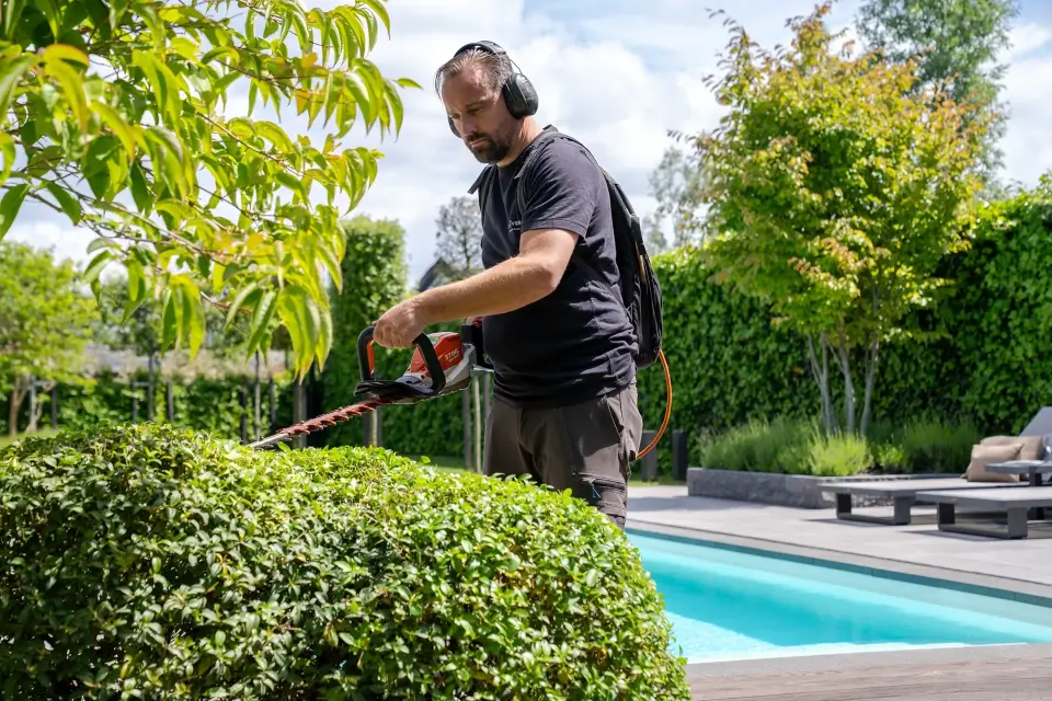 Hovenier van Art Verde snoeit haag bij luxe tuin met zwembad tijdens professioneel onderhoud