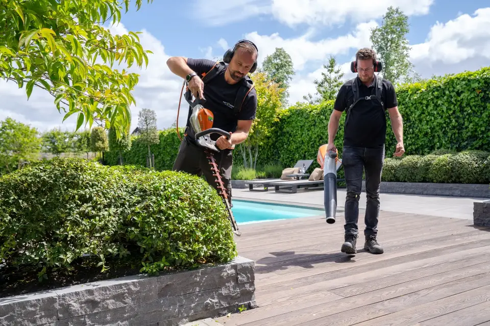 Twee hoveniers van Art Verde voeren professioneel tuinonderhoud uit bij een luxe tuin met zwembad